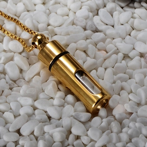 Gold cylindrical essential oil bottle necklace with clear window on white pebbles