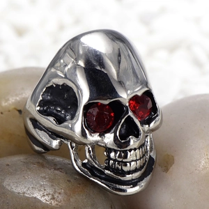 Retro stainless steel skull ring with red rhinestone eyes on light pebble background