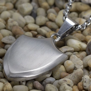 Macro shot of brushed stainless steel shield pendant on smooth river stones