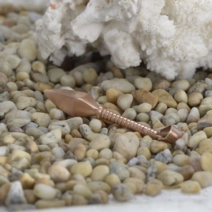 Dettaglio macro del ciondolo a lancia kunai oro rosa su pietre naturali di fiume