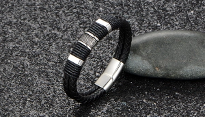 Detail shot of black braided leather bracelet with silver magnetic clasp on dark pebbles