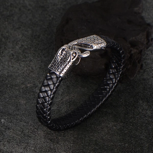 Punk black woven leather bracelet featuring a silver metal snake head clasp on rock background