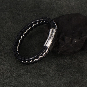 Men's black braided leather bracelet with a polished silver magnetic clasp on a stone background