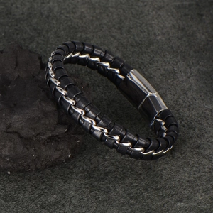 Braided black leather men's bracelet with silver metal chain on a dark rock background