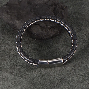 Detail of men's black woven leather bracelet with matte steel clasp on rock surface