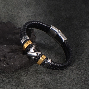 Men's woven leather bracelet with silver metal cross charm and gold rings on stone