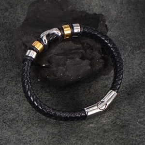 Braided black leather men's bracelet with gold and silver steel rings on stone background