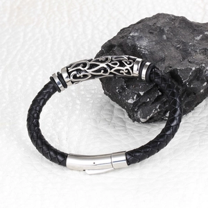 Detail of black braided leather bracelet with silver tribal pattern metal charm and clasp