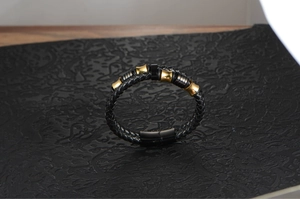 Detail of black braided leather bracelet featuring gold and black metal cylinders