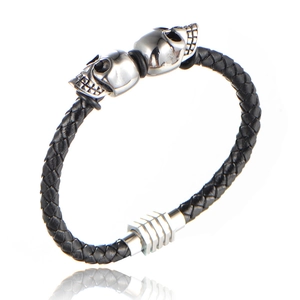 Detail view of woven black leather bracelet with silver skull charms and gear-style clasp