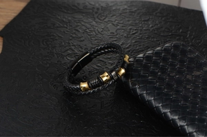 Close-up of double-layer black braided leather bracelet with gold and black metal charms