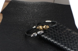 Close-up of black braided leather bracelets with gold and silver skull steel charms