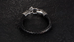 Macro shot of silver dragon head terminals on braided black leather bracelet with ring clasp