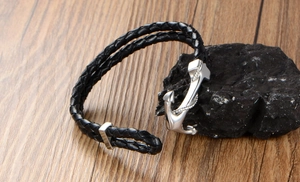 Detail of nautical anchor clasp on black braided leather bracelet over dark rock