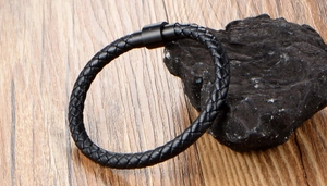 Close-up of black braided leather bracelet with matte metal magnetic clasp on wooden desk