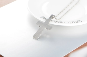 Close-up of brushed stainless steel triple cross pendant with rounded edges and bead chain