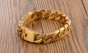 Detail of a matte gold Cuban link bracelet with square clasp on a wood background