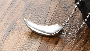 Detailed view of silver wolf tooth pendant made of stainless steel on wooden background