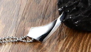 Macro shot of silver polished wolf tooth pendant on a ball chain over dark natural wood