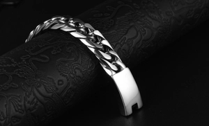 Detail of silver Cuban link bracelet with smooth rectangular clasp on black textured stand