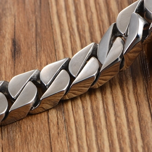 Polished silver stainless steel curb chain bracelet on a wooden background