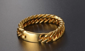 Detail of gold Cuban link bracelet with a polished rectangular clasp on a textured surface