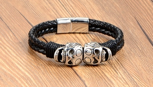 Close-up of black braided leather men's bracelet with silver skull charms and magnetic clasp