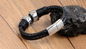 Detail of woven black leather bracelet with silver skull metal charms and magnetic clasp