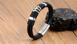 Détail d'un bracelet en cuir noir tressé avec des anneaux en métal argenté sur bois
