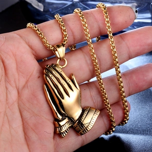Golden stainless steel praying hands pendant on box chain held by hand for size reference