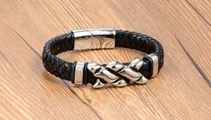 Macro detail of men's black braided leather bracelet with flame-shaped steel charm