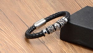 Detail of black braided leather bracelet with silver skull charm on wood background