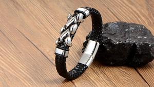 Detail of woven black leather bracelet with flame-style metal charm and magnetic clasp