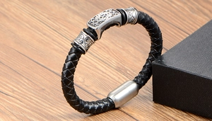 Detail view of woven black leather bracelet with vintage floral engraved metal charms