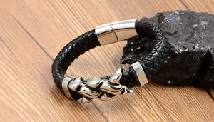 Macro shot of a men's black braided leather bracelet with a silver claw charm on wood