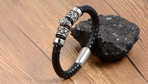Detail of woven black leather bracelet featuring a silver skull charm on a dark stone