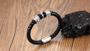 Macro shot of men's leather skull bracelet with fleur-de-lis charms on wood surface