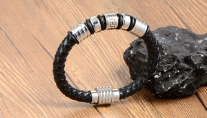 Close-up of black braided leather bracelet with silver Greek meander pattern charm