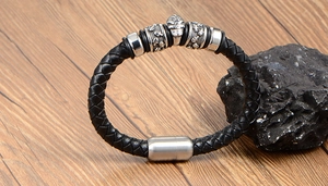 Close-up of braided black leather bracelet featuring metallic skulls and magnetic clasp