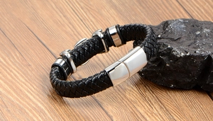 Detail of woven black leather bracelet with silver magnetic clasp on rustic wood