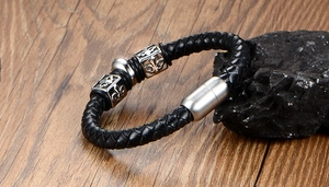 Macro shot of men's braided leather bracelet with fleur-de-lis metal charms and magnetic clasp