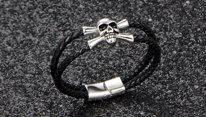 Detail of hand-woven black leather bracelet featuring silver skull charm and magnetic clasp