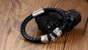 Detail of men's black braided leather bracelet with silver fleur-de-lis metal charms