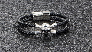 Detail of black woven leather men's bracelet featuring a silver skull and magnetic clasp