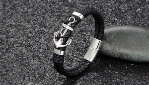 Detail of black braided leather bracelet with silver anchor charm on dark stone