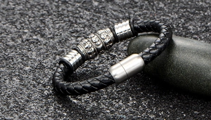 Détail d'un bracelet en cuir tressé noir avec fermoir magnétique et gravures de croix