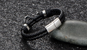 Close-up of double-layer black braided leather bracelet with silver anchor charm on stones
