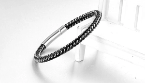 Detailed close-up of woven black leather and silver fiber bracelet with magnetic metal clasp