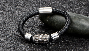 Gros plan du bracelet en cuir tressé avec perle de crâne argentée sur pierre sombre