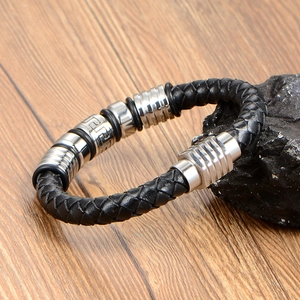 Braided black leather bracelet for men with silver Greek key pattern charms on wood background